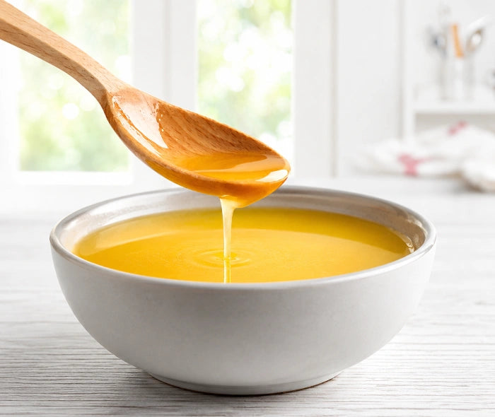 Flüssiges Ghee in einer Schale mit Holzlöffel